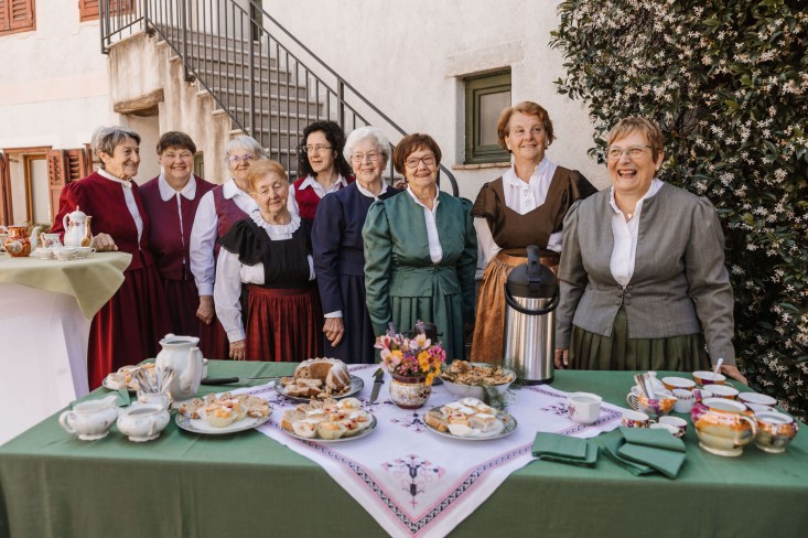 Skupina žensk iz Dornberka v tradicijskih narodnih nošah in oblekah stoji ob mizi s kavo, potico in pecivom na prostem.
